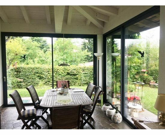 Bīdāmās ārdurvis izveidotas no alumīnija profiliem un stikla paketēm ar skatu no telpas iekšpuses uz zaļu ainavu